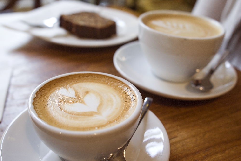 Two cups of coffee with a cake in the background