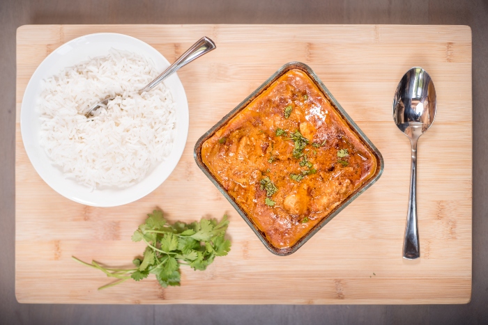 Jaisenes Chicken Curry Recipe sitting next to a bowl of rice in an ovenproof dish