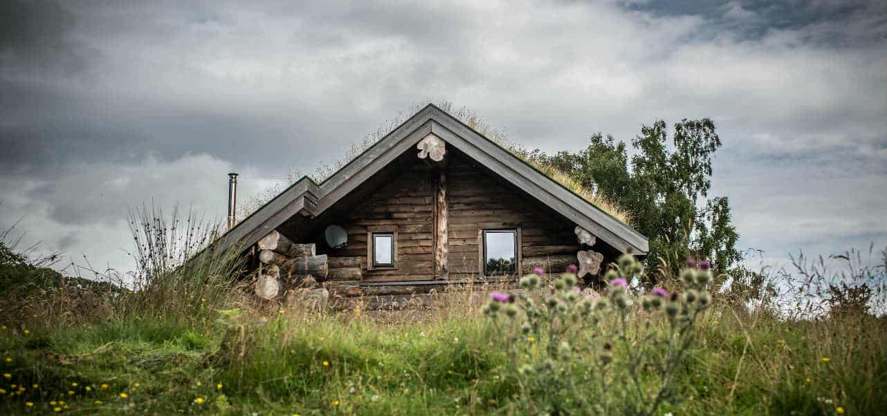 Log cabin peaking over a grassy hill with heavy clouds in the background