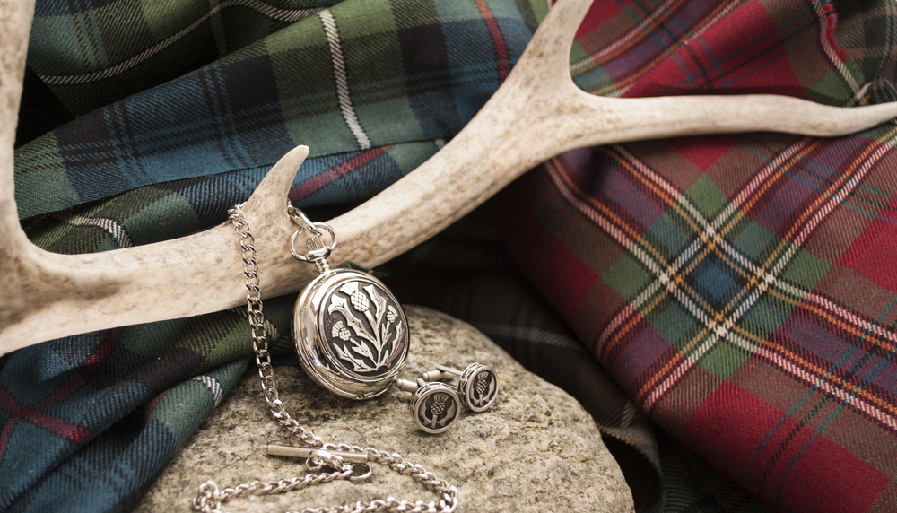 Scottish watch with chain and cufflinks with thistle design on tartan background.