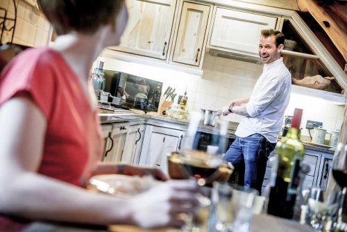 Man cooking in kitchen and woman sat at the table