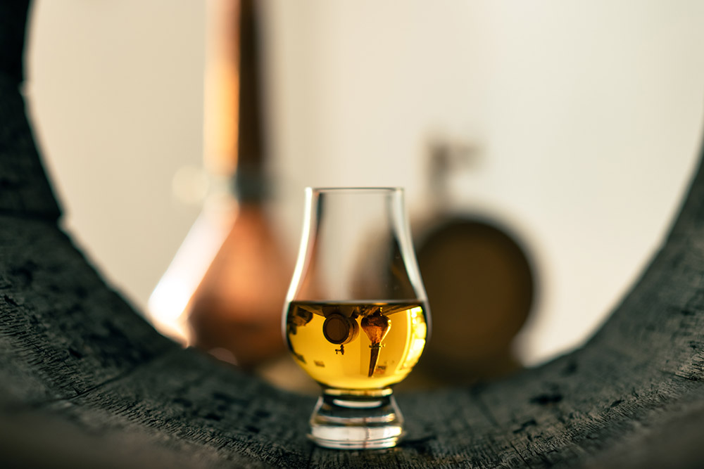 A glass of whisky in front of a distillery.